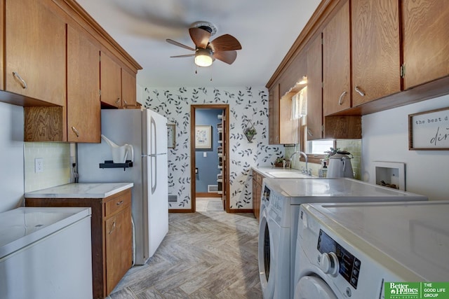 kitchen featuring brown cabinets, a sink, washing machine and dryer, freestanding refrigerator, and ceiling fan