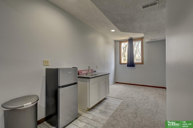 kitchen featuring visible vents, freestanding refrigerator, baseboards, a textured ceiling, and white cabinetry