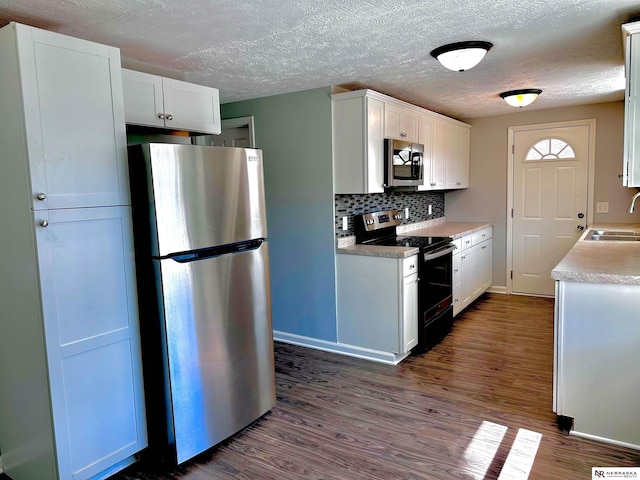 kitchen featuring white cabinets, stainless steel appliances, backsplash, a sink, and dark wood-type flooring