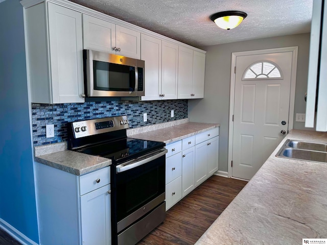kitchen featuring a sink, dark wood-style flooring, white cabinetry, backsplash, and appliances with stainless steel finishes