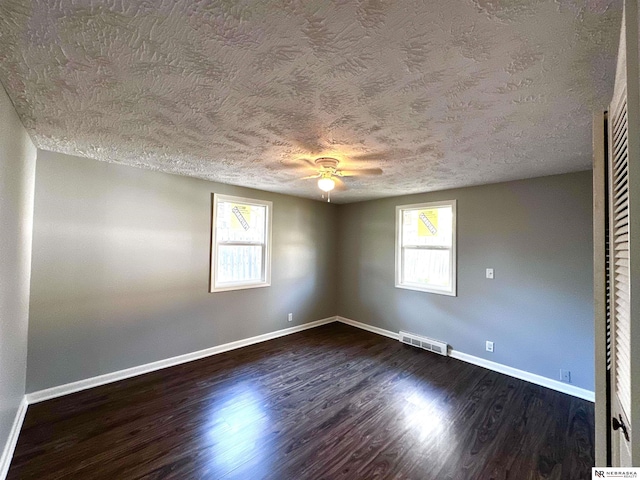 empty room featuring a textured ceiling, ceiling fan, dark wood finished floors, baseboards, and visible vents