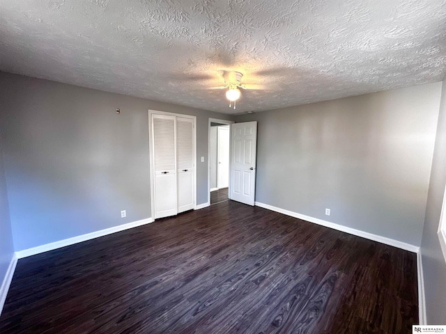 unfurnished bedroom featuring a ceiling fan, a closet, baseboards, a textured ceiling, and dark wood-style flooring