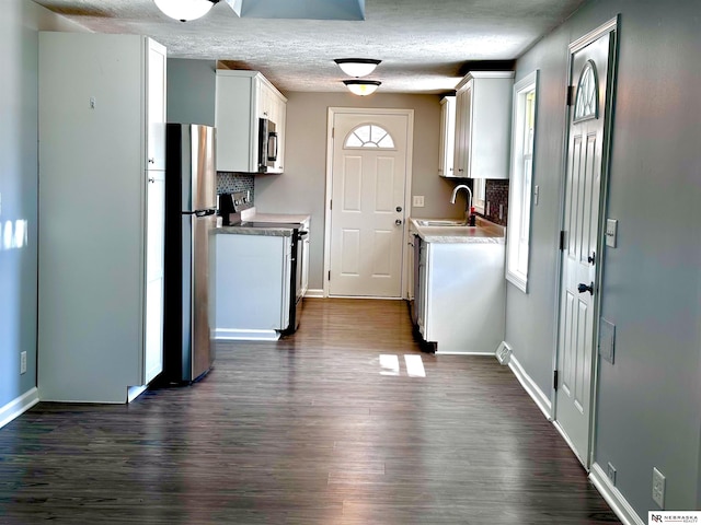kitchen with a sink, decorative backsplash, appliances with stainless steel finishes, baseboards, and dark wood-style flooring