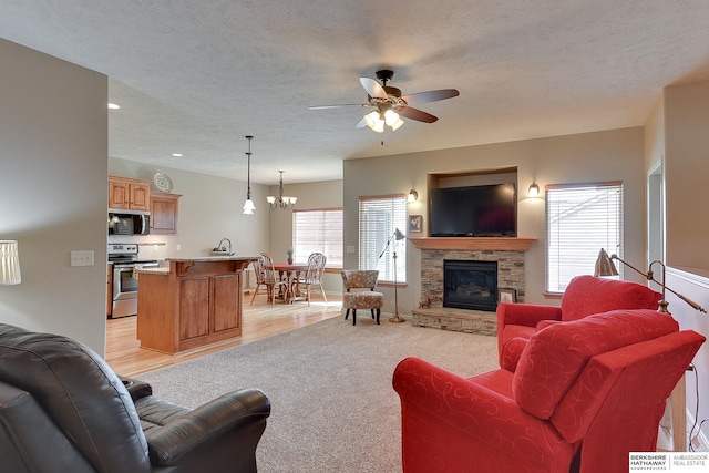 living area featuring recessed lighting, a fireplace, light wood-style flooring, a textured ceiling, and ceiling fan with notable chandelier