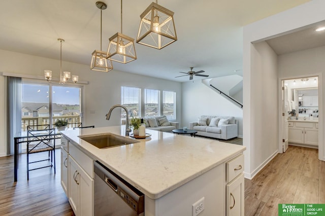 kitchen with light wood finished floors, stainless steel dishwasher, a sink, white cabinetry, and ceiling fan with notable chandelier