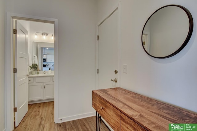 corridor featuring baseboards, a sink, and light wood-style flooring