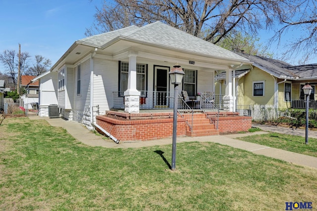 bungalow-style house with roof with shingles, a front yard, and fence