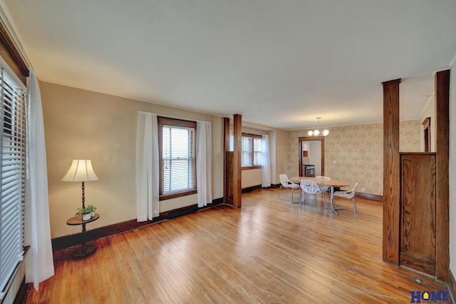 living room featuring wallpapered walls, light wood-type flooring, baseboards, and a notable chandelier