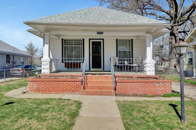 view of front of house with a shingled roof, covered porch, and fence