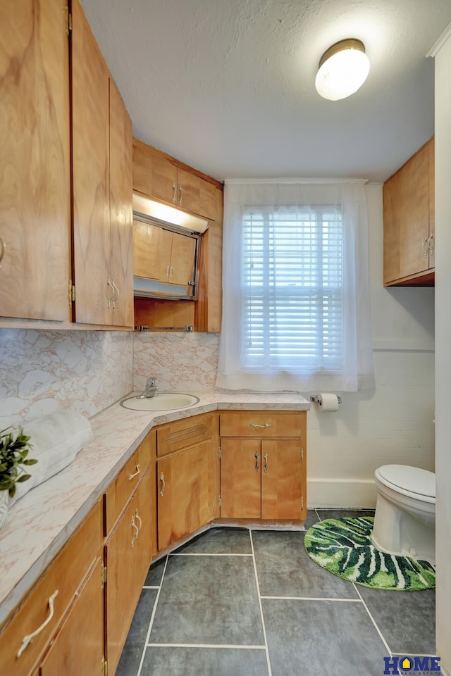 kitchen with a sink, tasteful backsplash, baseboards, light countertops, and dark tile patterned floors