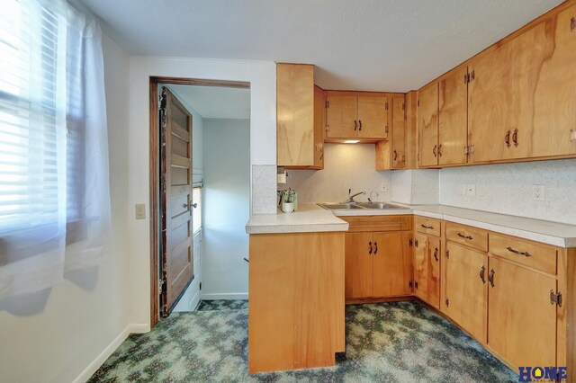kitchen with a sink, tasteful backsplash, baseboards, dark carpet, and light countertops