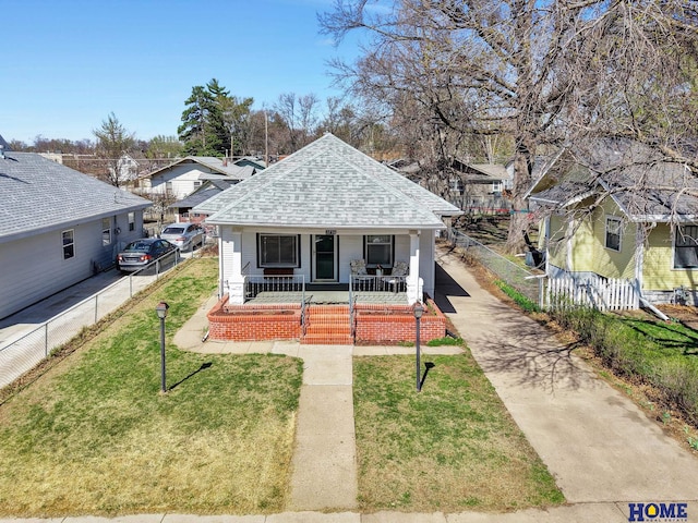 bungalow-style house featuring a front lawn, fence, a porch, and a shingled roof