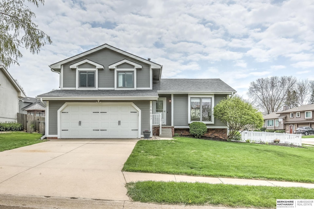 split level home featuring an attached garage, fence, driveway, and a front yard