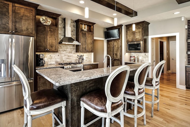 kitchen with stainless steel appliances, tasteful backsplash, a breakfast bar area, and wall chimney range hood
