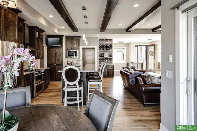 kitchen featuring wall chimney range hood, stainless steel appliances, beamed ceiling, and light wood-type flooring
