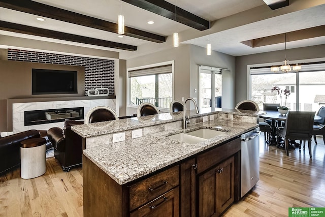kitchen featuring light wood-style flooring, a sink, open floor plan, light stone counters, and dishwasher