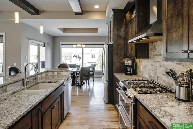 kitchen featuring stainless steel appliances, light wood-style flooring, a sink, wall chimney range hood, and decorative light fixtures
