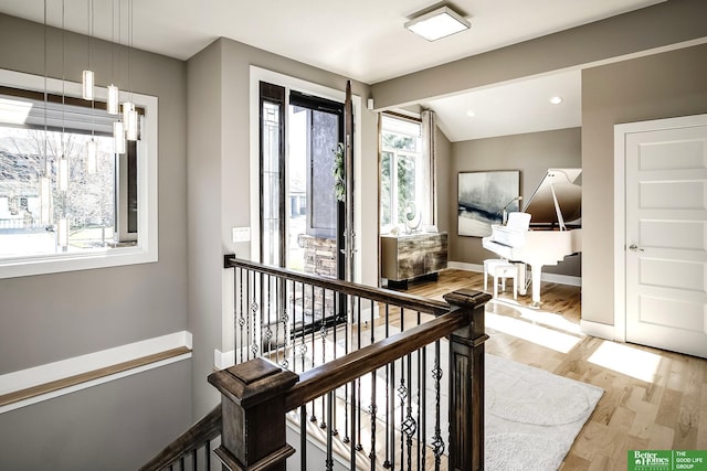 hall featuring light wood-style floors, baseboards, and an upstairs landing
