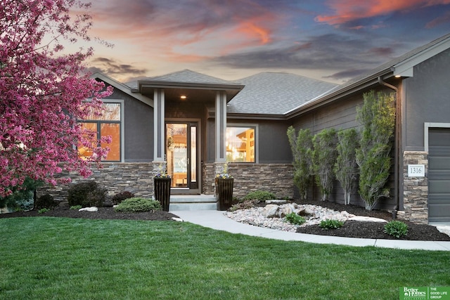 prairie-style home featuring stone siding, a lawn, a shingled roof, and stucco siding