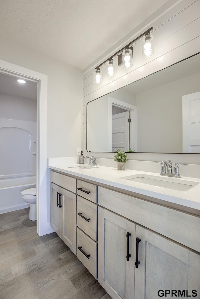 full bathroom with wood finished floors, a sink, double vanity, and toilet
