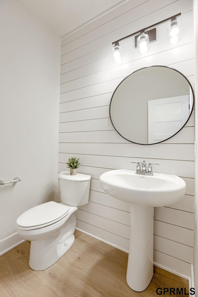 half bath featuring wood finished floors, toilet, baseboards, and wood walls