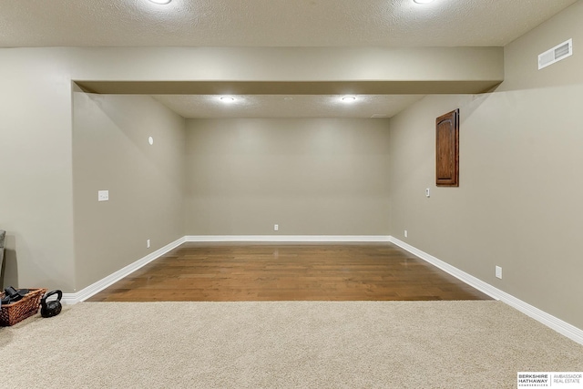 finished basement with carpet flooring, a textured ceiling, visible vents, and baseboards