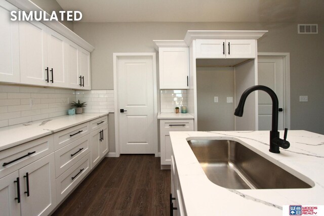 kitchen with white cabinets, dark wood-style floors, a sink, light stone countertops, and tasteful backsplash