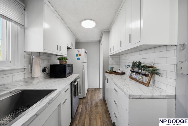 kitchen featuring black microwave, stainless steel dishwasher, white cabinetry, and tasteful backsplash