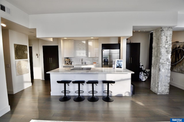 kitchen with light countertops, visible vents, a sink, stainless steel fridge, and a breakfast bar area