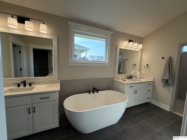 full bathroom featuring two vanities, a soaking tub, tile patterned flooring, and a sink