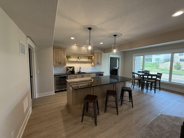 kitchen with beverage cooler, dark countertops, a kitchen bar, a sink, and visible vents