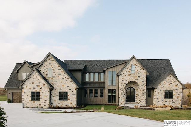 view of front facade with board and batten siding, driveway, stone siding, and roof with shingles