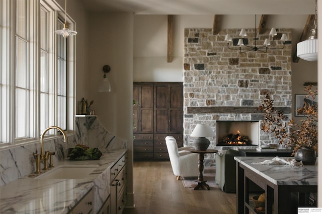 kitchen with wood finished floors, a stone fireplace, a sink, light stone countertops, and beam ceiling