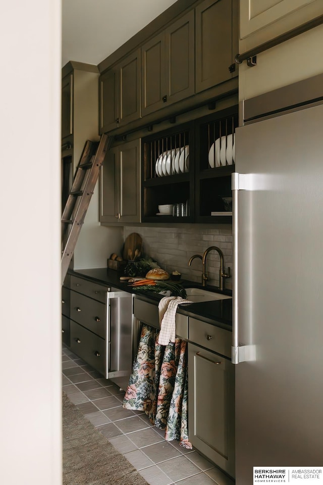 bar featuring backsplash, stainless steel refrigerator, dark tile patterned flooring, and a sink