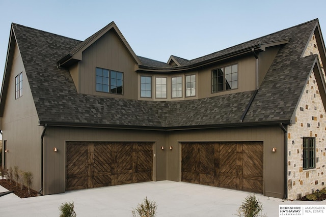 view of front facade with an attached garage, roof with shingles, stone siding, and driveway