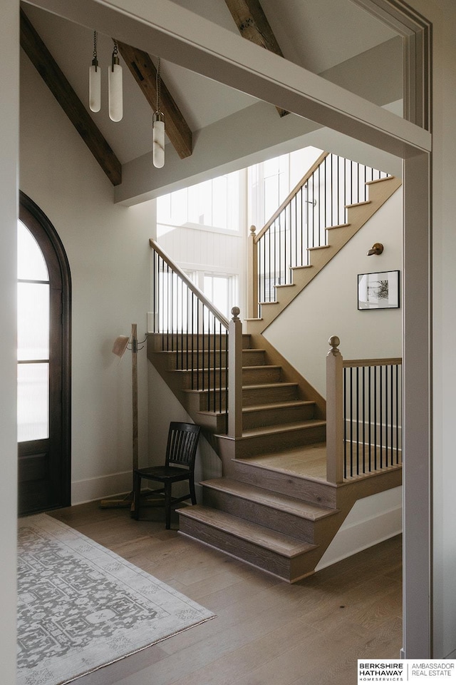 stairway with wood finished floors, beam ceiling, baseboards, and a high ceiling