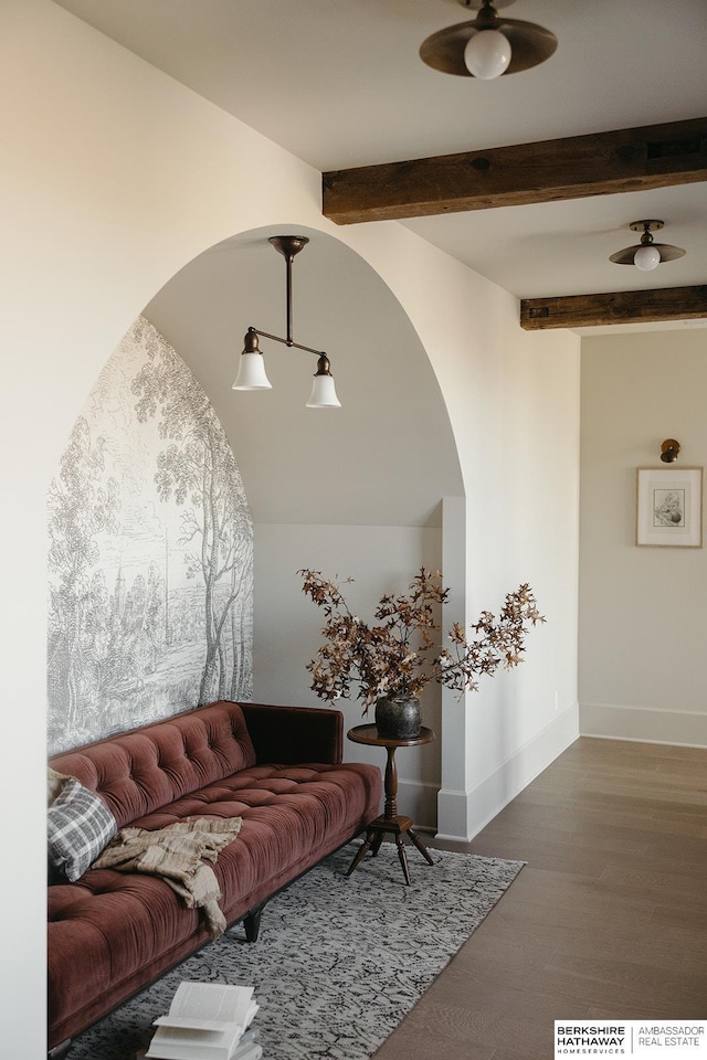 living area with a ceiling fan, wood finished floors, arched walkways, beamed ceiling, and baseboards