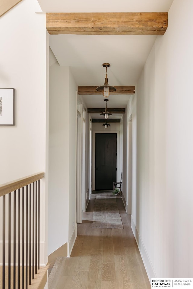 corridor featuring baseboards, beam ceiling, and light wood finished floors