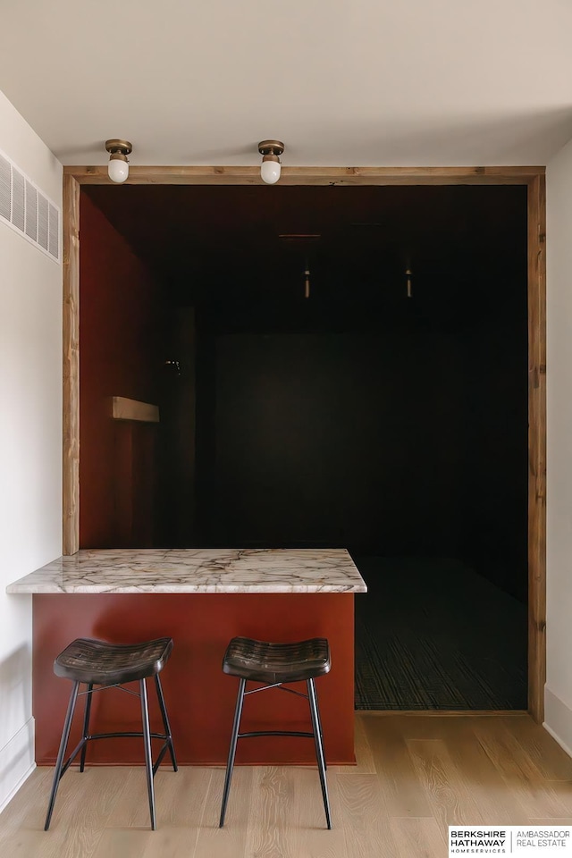 interior space with light stone counters, a breakfast bar, light wood finished floors, a peninsula, and visible vents