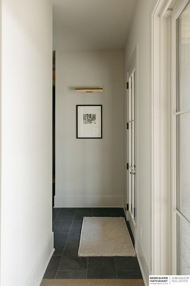 corridor featuring baseboards and dark tile patterned flooring