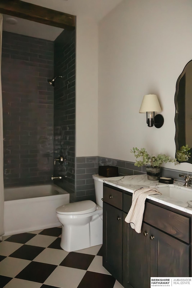 full bathroom with tile patterned floors, a wainscoted wall,  shower combination, toilet, and vanity