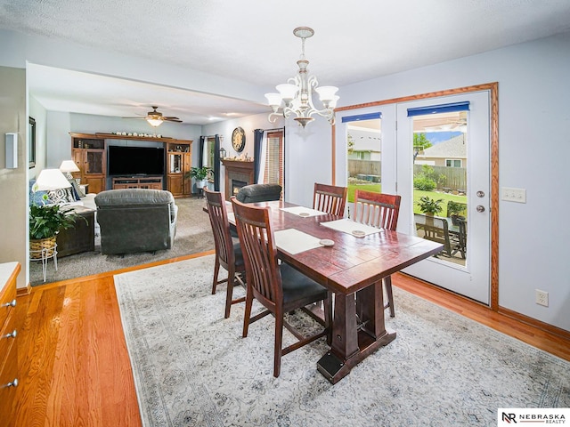 dining area featuring wood finished floors, ceiling fan, a chandelier, a warm lit fireplace, and baseboards