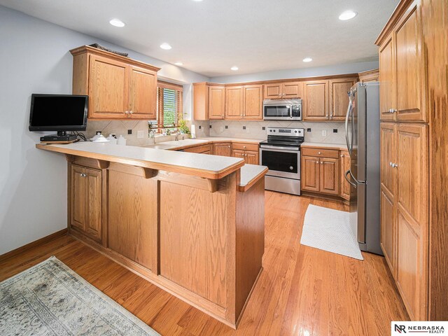kitchen with stainless steel appliances, a peninsula, decorative backsplash, light wood-type flooring, and light countertops