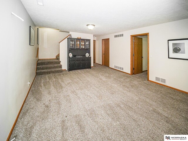 unfurnished living room featuring baseboards, stairs, and carpet floors