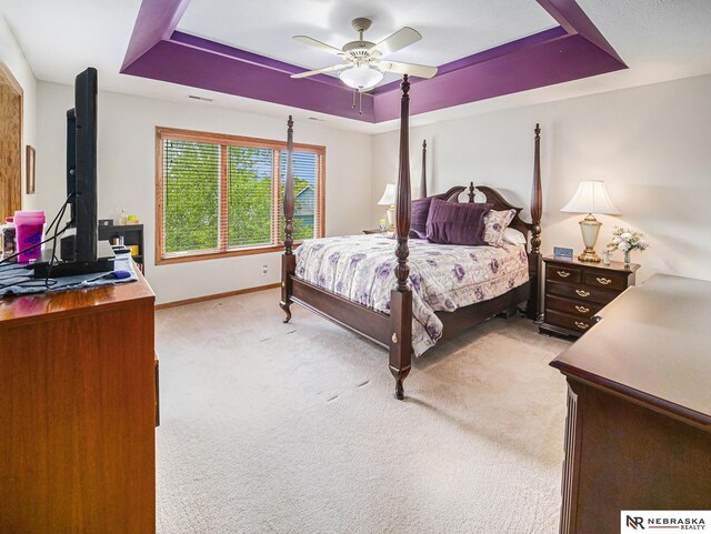 bedroom featuring a raised ceiling, baseboards, light colored carpet, and a ceiling fan