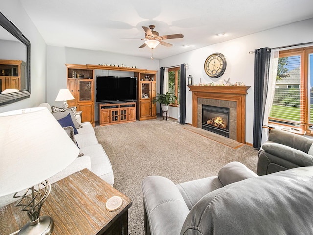 living area with carpet flooring, ceiling fan, a tiled fireplace, and baseboards