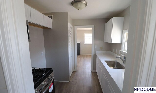 kitchen featuring white cabinets, stainless steel range with gas cooktop, a sink, baseboards, and wood finished floors