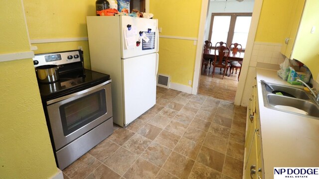 kitchen featuring visible vents, a sink, freestanding refrigerator, stone finish flooring, and stainless steel electric range