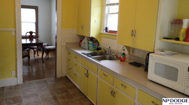kitchen featuring yellow cabinets, light countertops, a sink, and white microwave