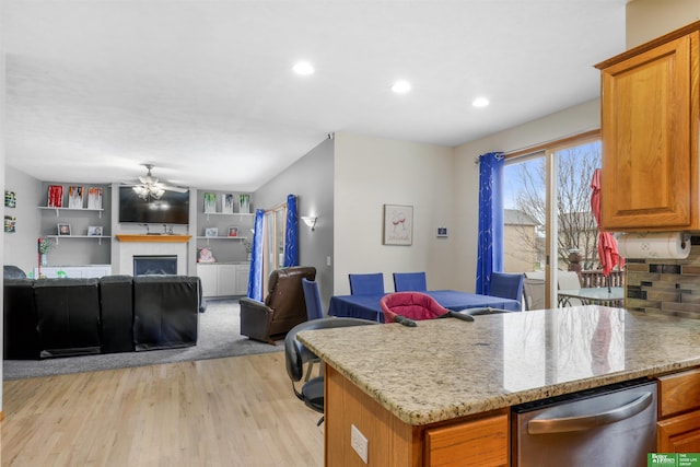kitchen with a ceiling fan, brown cabinetry, open floor plan, light wood finished floors, and a fireplace